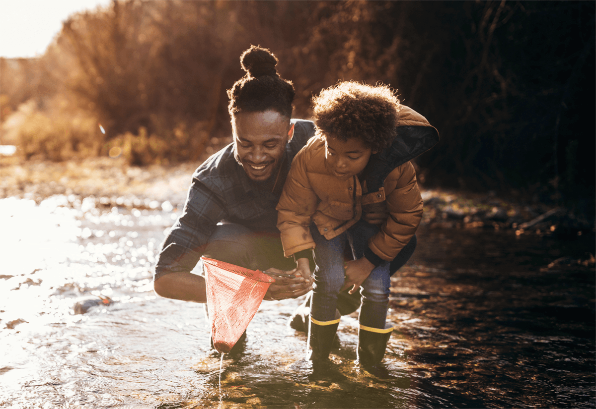 En person och ett barn står i ett vattedrag och letar saker med håv